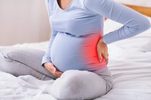 Pregnant Lady Touching Back Sitting On Bed to symbolize pregnancy and back pain