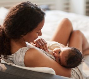 High angle portrait of young African-American mother breastfeeding cute baby boy with child looking at camera