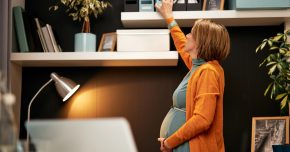 Side view of a pregnant woman in office, touching belly and trying to reach binder to represent pregnancy myths