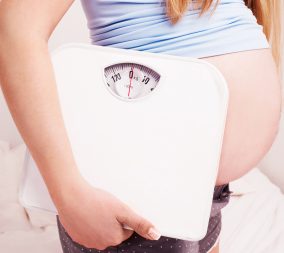 a pregnant woman holding a scale to symbolize weight gain in pregnancy