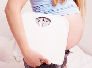 a pregnant woman holding a scale to symbolize weight gain in pregnancy