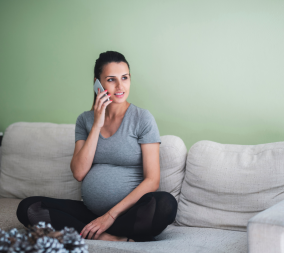 A woman sin her third trimester sitting on the couch talking on her cell phone