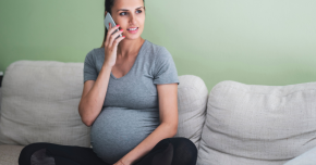 A woman sin her third trimester sitting on the couch talking on her cell phone