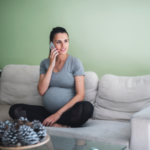 A woman sin her third trimester sitting on the couch talking on her cell phone