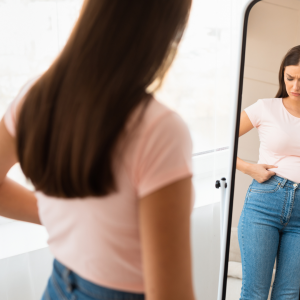 A woman looking in the mirror thinking she is too fat for sex