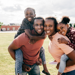 A mom and dad giving their son and daughter a piggy back to represent the outcome of natural family planning