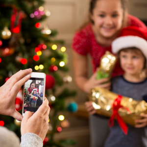 An iphone taking a photo of two kids in front of a christmas tree to represent photographing your children