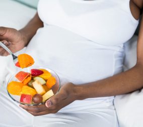 a pregnant woman eating healthy fruit salad