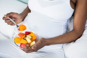 a pregnant woman eating healthy fruit salad