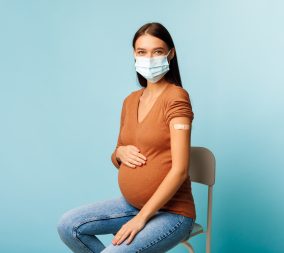 a pregnant woman wearing a mask with a bandaid on her arm after a vaccine to represent the importance of Covid vaccine in pregnancy
