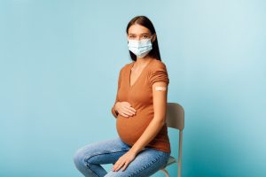 a pregnant woman wearing a mask with a bandaid on her arm after a vaccine to represent the importance of Covid vaccine in pregnancy