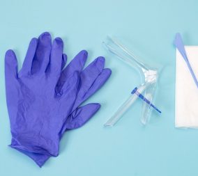 An overhead photo of the vaginal speculum, white napkin, medicine gloves and spatula. Medical plastic tool for holding open the vagina during medical investigation. Feminine woman health diagnosis. Image used to relay the updates to pap smear guidelines.