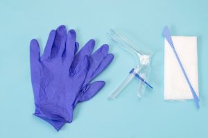 An overhead photo of the vaginal speculum, white napkin, medicine gloves and spatula. Medical plastic tool for holding open the vagina during medical investigation. Feminine woman health diagnosis. Image used to relay the updates to pap smear guidelines.