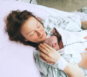 Mother holding her newborn baby child after induction of labor in a hospital.