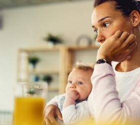 Young woman suffering from postpartum depression and thinking of something while being with her baby at home.