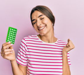 Young hispanic woman holding birth control pills screaming proud, celebrating victory and success very excited with raised arm