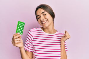 Young hispanic woman holding birth control pills screaming proud, celebrating victory and success very excited with raised arm